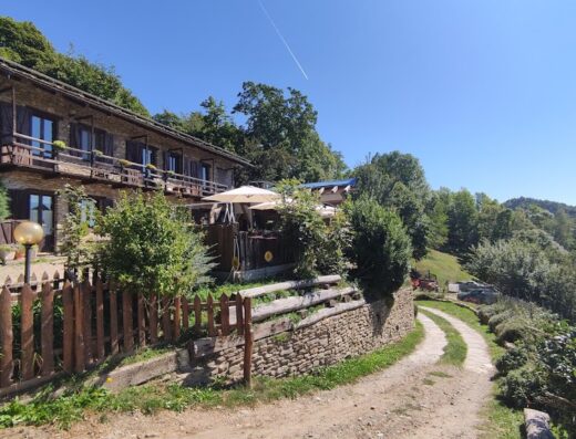 Agriturismo Fiorendo: Facciata esterna in pietra con balconi in legno, ombrelloni e sentiero sterrato in una giornata di sole.