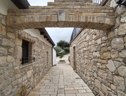 Passaggio pedonale ad Agriturismo Fontefredda, con arco in pietra, pavimentazione in lastre e muri in pietra a vista.