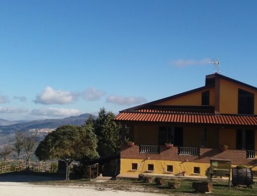 Agriturismo Forgione: vista esterna della struttura con cielo azzurro, colline sullo sfondo, ideale per un soggiorno rilassante e una vacanza in moto.