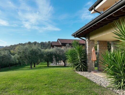 Agriturismo Garda Hill: Vista panoramica con uliveto, prato verde e struttura in pietra, ideale per un soggiorno rilassante.