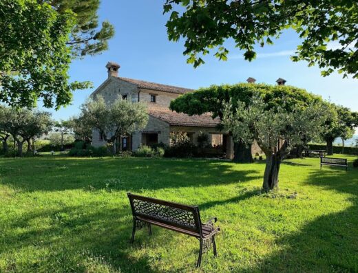 Agriturismo I Mori: Casale in pietra con giardino verde curato, ulivi e panchine in ferro battuto, tipico della campagna italiana.