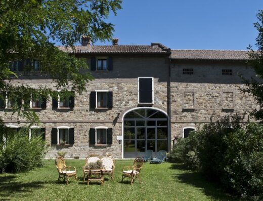 Agriturismo Il Brugnolo: External view of stone farmhouse with lawn, wicker chairs and table, offering a relaxing travel stay.