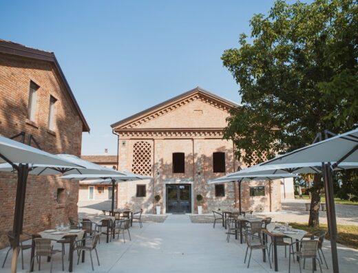 Agriturismo Il Capitolo: Exterior view of the farmhouse with outdoor dining area set with tables and chairs under umbrellas.