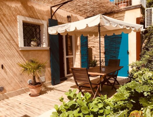 Patio area at Agriturismo Il Cardo del Lago with wooden table, chairs, sun umbrella, potted plant, and blue shutters.