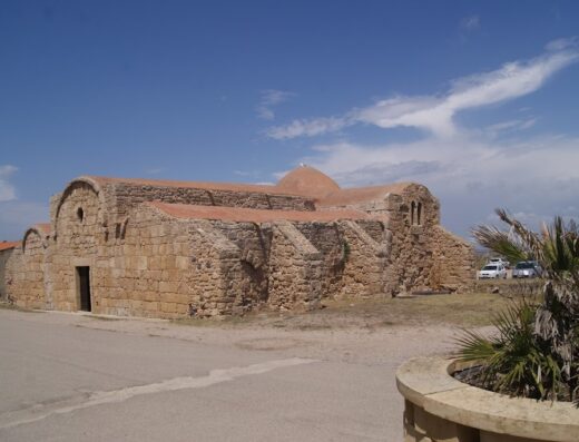 Agriturismo Il Sinis: Esterno dell'antica chiesa di San Giovanni di Sinis, con struttura in pietra arenaria, tetto rosso e cielo azzurro.