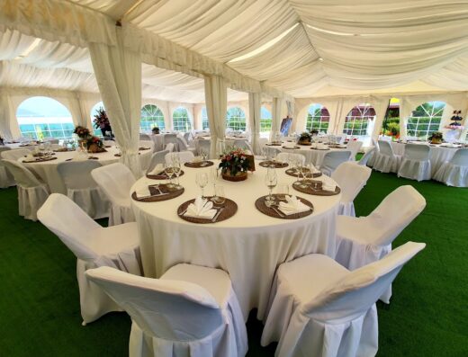 Interno di una location per eventi all'Agriturismo Il Timo, con tavoli rotondi apparecchiati, sedie rivestite di bianco e decorazioni floreali.