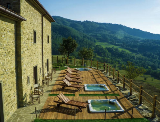 Agriturismo Incisa vista esterna: edificio in pietra, solarium in legno con lettini e vasche idromassaggio, colline sullo sfondo