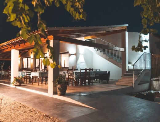 Agriturismo Irghitula's outdoor dining area at night, featuring tables set for dinner, stairs to an upper level, and ambient lighting, perfect for a relaxing travel experience.