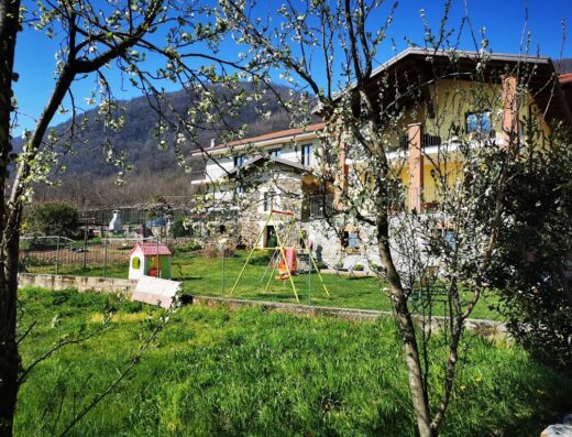 Agriturismo La Ca' d'Amelio: Veduta esterna dell'agriturismo con giardino, area giochi per bambini e montagne sullo sfondo.