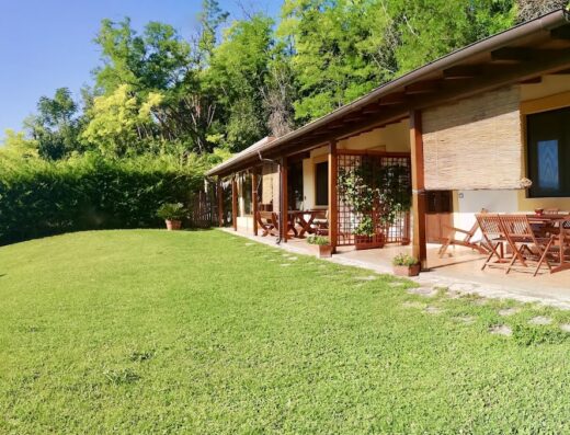 L'esterno curato dell'Agriturismo La Casa Nettarina, con prato verde, portico in legno arredato con tavoli e sedie, ideale per un soggiorno rilassante nella natura.