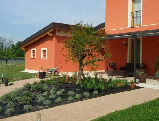 Agriturismo La Chiocciola garden view with terracotta buildings, stone pathways, planted flower beds, and patio seating.