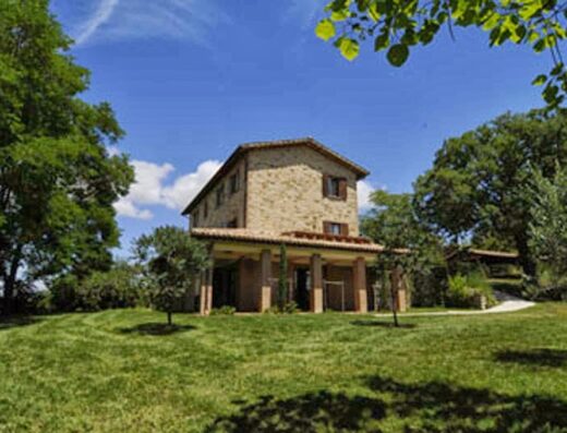 Agriturismo La Corte Del Lupo, Italia: Vista esterna della struttura in pietra con portico, circondata da un ampio giardino verde e alberi.