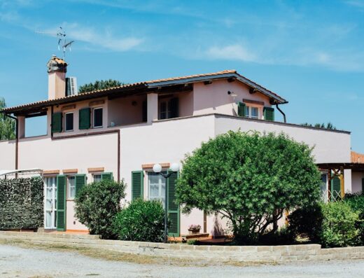 Agriturismo La Quercia, a charming farmhouse with a pool in the Tuscan seaside near Grosseto, featuring a pink building with green shutters and lush greenery.
