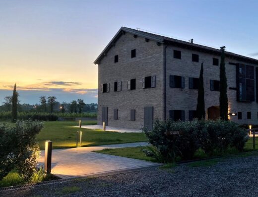 Agriturismo La Razza al tramonto: elegante casale in mattoni con persiane aperte, prato curato e luci soffuse, un'oasi di relax e natura.