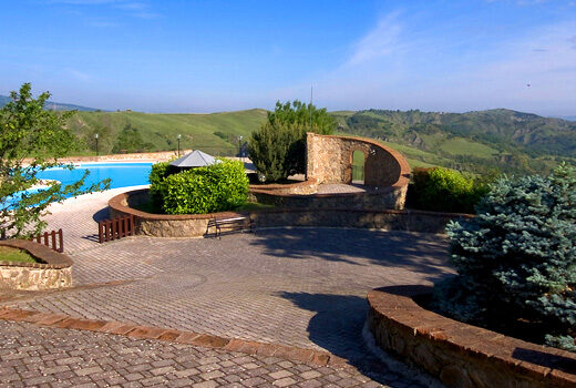 Agriturismo La Selvella panorama con piscina, colline verdi, area relax e vialetto in pietra, ideale per vacanze e turismo rurale in Italia