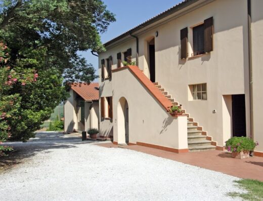 Agriturismo La Serra building exterior with stone pathway, stairs to upper level, and lush green plants, showcasing rural Italian travel.