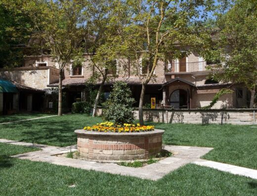 Agriturismo La Sfruscià Resort: Fioriera circolare in mattoni con fiori gialli nel giardino curato della struttura ricettiva.