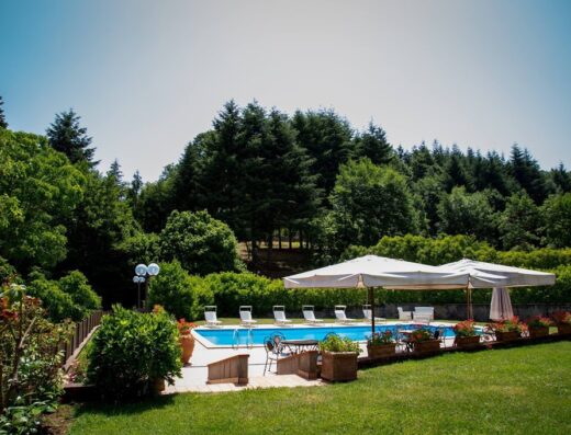 Piscina rilassante all'Agriturismo La Vecchia Fattoria, circondata da verde lussureggiante, ombrelloni bianchi e sedie a sdraio per un'esperienza di vacanza indimenticabile.