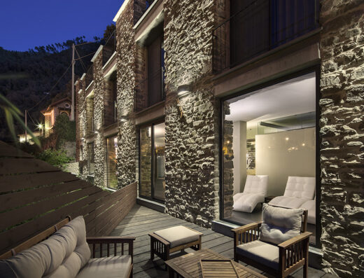 Agriturismo L'Adagio: Esterno in pietra illuminato di sera con terrazza in legno arredata e vista su interni di design.