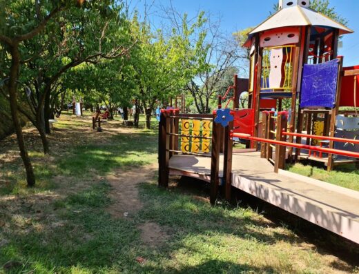 Area giochi per bambini all'Agriturismo L'Ape Regina, con struttura colorata e spazio verde alberato per il divertimento all'aperto.