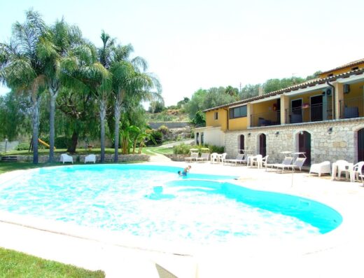 Agriturismo Le Chiuse swimming pool view, with palm trees, sun loungers, and a child in the pool, providing a relaxing vacation experience.