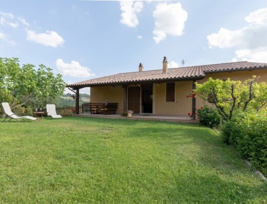 Agriturismo Le Dolci Colline: Exterior view of the farmhouse, showcasing a lush green lawn, patio with seating, and sun loungers, perfect for a relaxing travel experience in the Italian countryside.