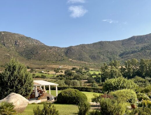 Agriturismo Li Teggi: vista panoramica sulla campagna sarda con giardino curato, gazebo e sullo sfondo le montagne.