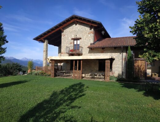 Agriturismo Locanda Cá Del Pian: A stone building with a balcony, patio, and a lush green lawn, showcasing the rustic charm of this Italian farmhouse.