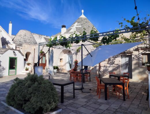 Agriturismo Masseria Catucci: Vista esterna con trulli tradizionali, tavoli e sedie per la ristorazione, pergolato con viti, atmosfera accogliente.