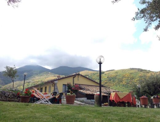 Agriturismo Masseria Senise Pollino: Vista esterna della masseria con tavoli apparecchiati, sedie a sdraio e montagne sullo sfondo, ideale per viaggi e relax.