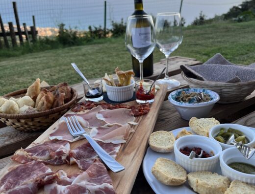 Tavola imbandita con salumi, formaggi, pane e vino presso l'Agriturismo Mendicino, Calabria, con vista panoramica sul mare al tramonto.
