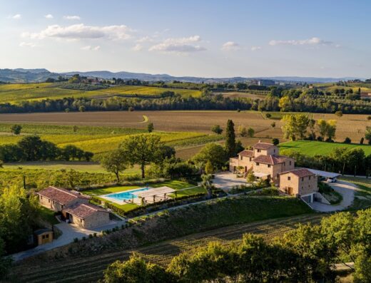 Vista aerea dell'Agriturismo Merigge Wellness & Spa, un casale toscano con piscina immerso nel paesaggio collinare, tra campi coltivati e vigneti.