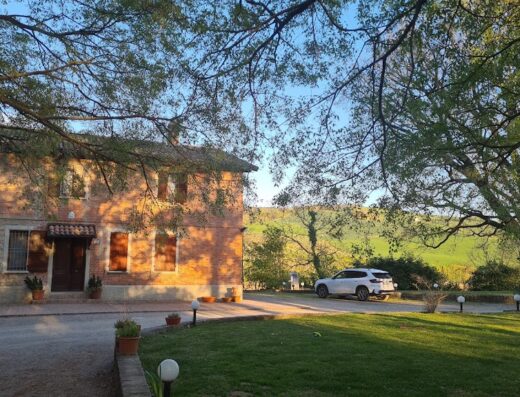 Agriturismo Molino Nuovo: A charming brick farmhouse with a white car parked nearby, surrounded by green fields and trees.