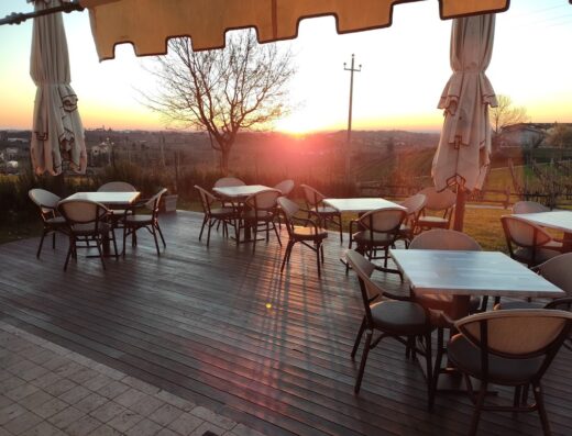 Terrazza panoramica all'Agriturismo Moro Barel al tramonto, con tavoli e sedie pronti per accogliere gli ospiti per un'esperienza culinaria indimenticabile.