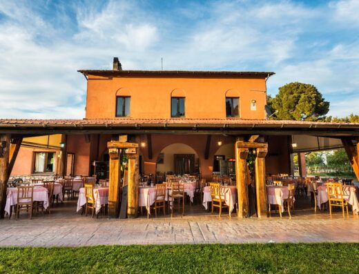 Agriturismo Podere Del Gesso: Exterior view of the restaurant with outdoor seating, featuring wooden beams and tables with pink tablecloths, under a blue sky.