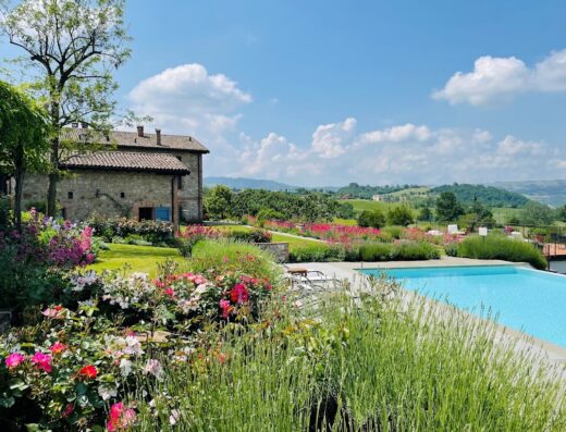 Agriturismo Podere Prasiano: Vista panoramica della piscina e del casale in pietra circondato da un giardino fiorito, ideale per un soggiorno rilassante.