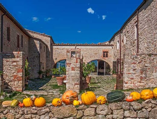 Agriturismo Podere Spedalone in Toscana con zucche decorative su un muro di pietra, cielo azzurro, architettura rustica.