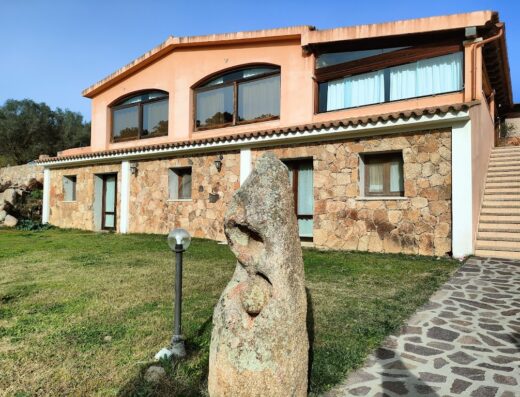 Agriturismo San Giovanni: Esterno della struttura con facciata in pietra, prato verde, scultura in pietra e cielo azzurro.