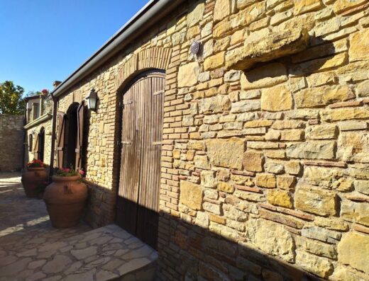 Agriturismo Sant'Agata: Facciata esterna in pietra con porta ad arco in legno, vasi di fiori e lampada da parete.