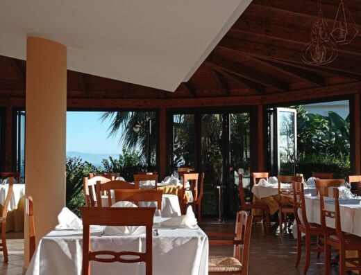 Interno del ristorante dell'agriturismo Seaview con tavoli apparecchiati, sedie in legno e vista panoramica sul mare dalla vetrata.