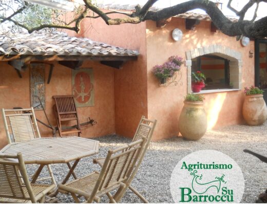 Agriturismo Su Barroccu in Sardegna con tavolo e sedie in bambù, vasi con fiori, finestra e dettagli architettonici tipici.