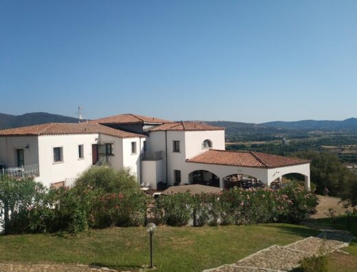 Agriturismo Su Vrau: Vista panoramica della struttura con architettura tipica sarda, giardino curato e paesaggio collinare sullo sfondo.