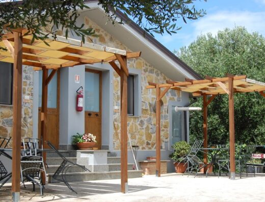 Agriturismo Tempa del Niglio: Esterno accogliente con pergolato in legno, tavoli e sedie in ferro battuto, facciata in pietra e porta d'ingresso in legno. Ideale per relax e viaggi.