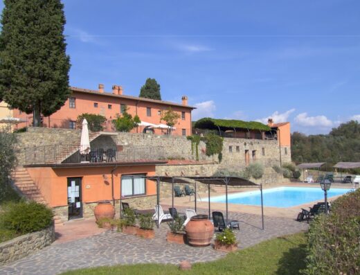 Agriturismo Tenuta Cantagallo: Vista della piscina e degli edifici in pietra, tipici dell'architettura toscana, sotto un cielo azzurro.