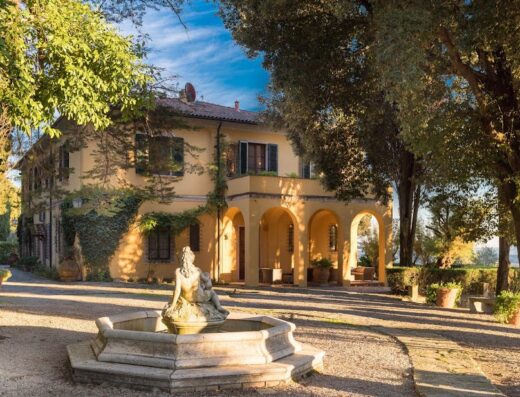 Agriturismo Tenuta La Bandita in Toscana: A charming country relais with a scenic view, featuring a classic Italian villa, arched entryway, and a beautiful stone fountain in the foreground. Ideal for a relaxing getaway in the Tuscan countryside.