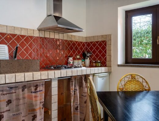 Interno della cucina rustica all'Agriturismo Tenuta Monte la Guardia, con piastrelle rosse, tavolo in legno scuro e finestra con vista sul verde.