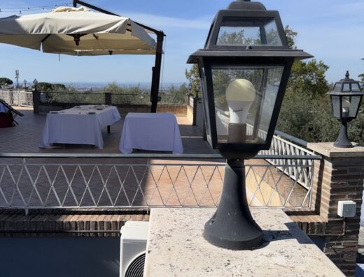 Terrazza panoramica all'Agriturismo Tenuta Quarto Santa Croce con lampione decorativo, tavoli apparecchiati e vista sul paesaggio circostante.