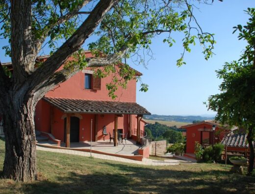 Agriturismo Tenuta San Savino delle Rocchette: vista esterna della struttura principale in pietra rossa con portico e giardino curato.