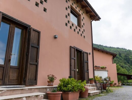 Agriturismo Terre Rosse Di Massadita exterior view with terracotta colored walls, wooden shutters and doors, potted plants, and a glimpse of the surrounding hills.