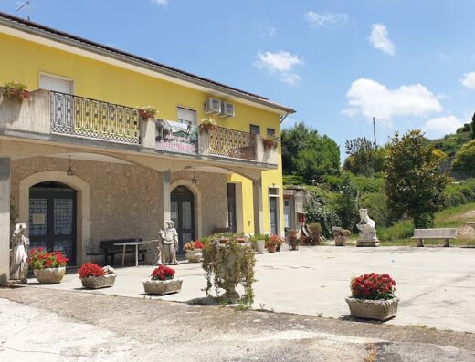 Agriturismo Torre di Magliano, Italy: View of the yellow building facade, featuring stone arches, statues, and flower-filled planters in a courtyard setting.